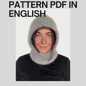 May include: A person wearing a gray crochet hood and cowl set. The image includes the text "CROCHET PATTERN PDF IN ENGLISH". The hood and cowl are made of a soft, textured yarn. The person is wearing a black shirt.