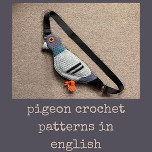 Puede incluir: Un bolso hecho a mano con forma de paloma de ganchillo con una correa negra. El ave presenta hilo gris, azul y negro, con patas y un ojo de color naranja. El texto "pigeon crochet patterns in english" está debajo.