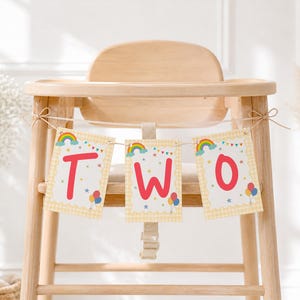 May include: A decorative banner featuring three rectangular cards tied to a wooden high chair. Each card displays a red letter spelling out the word TWO, accented with colorful rainbow, balloon, and star illustrations on a light yellow background.