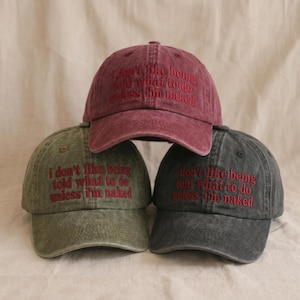 May include: Three baseball caps in maroon, olive green, and charcoal gray, each featuring a distressed fabric finish. The front of every cap is embroidered with the red text, "I don't like being told what to do unless I'm naked" in a serif font.
