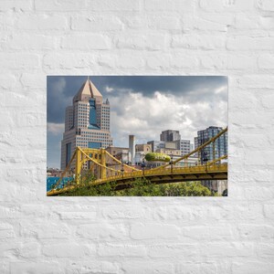 May include: A photograph of a cityscape featuring a yellow bridge with a sign that says "Heinz" and several tall buildings. The sky is overcast with dark clouds.
