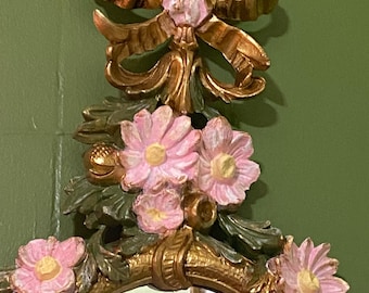 Un espejo de pared decorativo desgastado, con un diseño floral y flores rosas en relieve.
