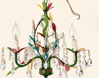 May include: A multi-colored metal chandelier featuring a green frame adorned with painted leaves in red, yellow, and blue. The fixture includes two candle-style light sockets and is decorated with numerous clear, faceted glass crystals.