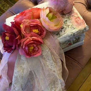 Puede incluir: Una caja blanca con diseño floral, decorada con flores rosas y rojas, una cinta rosa y una figurita de cerdo rosa.
