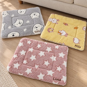Puede incluir: Tres alfombrillas rectangulares para mascotas con texturas de felpa. Una alfombrilla gris presenta caras de oso blancas y el nombre Teddy. Una alfombrilla amarilla muestra conejitos blancos y zanahorias con el nombre Milo. Una alfombrilla rosa tiene estrellas blancas y el nombre Luna.