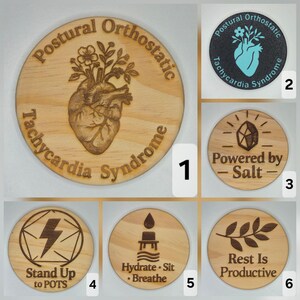 May include: A collection of wooden coasters with engraved designs and text. One coaster features a heart with flowers and the words "Postural Orthostatic Tachycardia Syndrome." Other coasters have phrases like "Powered by Salt" and "Rest Is Productive."