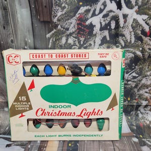 May include: Vintage box of Coast to Coast Stores indoor Christmas lights. The box features a green, white, and red color scheme with the text "Indoor Christmas Lights." The box contains 15 multi-colored lights, including green, blue, and yellow bulbs.