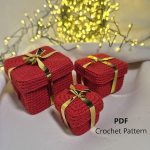 May include: Three red crocheted gift boxes of varying sizes, each adorned with a gold ribbon. The boxes are square-shaped and have a textured appearance. The text "PDF Crochet Pattern" is visible in the lower right corner.