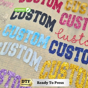May include: A collection of DTF transfer sheets featuring the word CUSTOM in various fonts, colors, and textures, including glittery pink, gold, blue, and matte black. A green RECOMMENDED badge and a DTF TRANSFER Ready To Press label are visible.