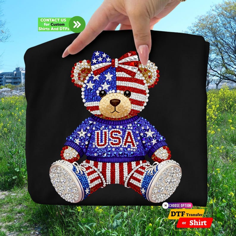 A sparkling faux rhinestone teddy bear design with American flag patterns on its face and bow, wearing a blue USA sweater and red-white striped pants. This high-quality patriotic DTF transfer and custom shirt option is perfect for the USA 250th anniversary celebrations, 4th of July parades, and Independence Day events. The 250 years of America commemorative graphic features a glittery diamond effect for a luxury look on black t-shirts and hoodies.