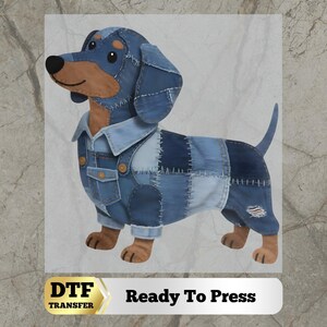 May include: A dachshund illustration featuring a patchwork denim outfit with visible stitching, a collar, and a pocket. The dog has brown fur on its face and legs, and the design includes the text DTF TRANSFER Ready To Press at the bottom.