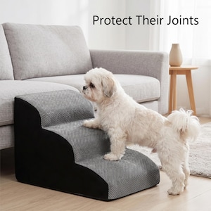 May include: A gray and black pet step with three steps, designed to help small dogs reach furniture. The steps have a textured surface and are positioned in front of a gray sofa. The text "Protect Their Joints" is visible.