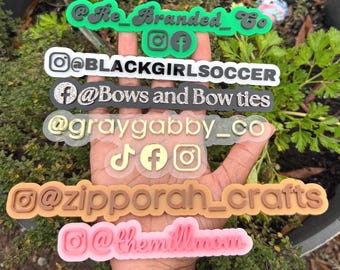 May include: A hand holds several colorful, translucent social media profile name tags. The tags are in various colors, including green, white, black, gold, brown, and pink. Each tag features a different name and social media icons, such as Instagram and Facebook.