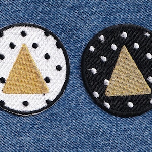 May include: Two circular embroidered patches. One patch features a white background with black polka dots and a central gold triangle. The second patch features a black background with white polka dots and a central gold triangle. Both have black borders.