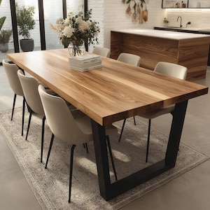 May include: A large, rectangular wooden dining table with a natural finish, supported by black metal legs. The table is surrounded by six beige upholstered chairs with black legs. A stack of books and a vase of flowers sit on the table. The table is set on a patterned rug.