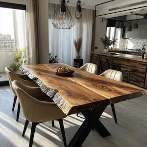 Könnte beinhalten: Ein großer Esstisch aus Holz mit natürlicher Kante und dunkler Oberfläche, getragen von einem schwarzen Metallgestell in X-Form. Der Tisch ist von beige gepolsterten Stühlen umgeben. Eine Schale mit Obst steht auf dem Tisch. Dekorative Beleuchtung hängt darüber.