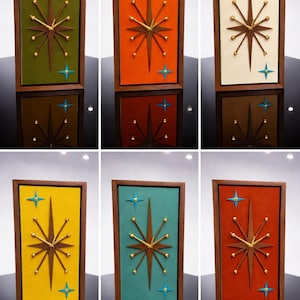 May include: A collection of mid-century modern wall clocks. Each clock features a starburst design with gold accents and blue star details, set against a colorful background within a wooden frame. The clocks are rectangular and have a retro aesthetic.