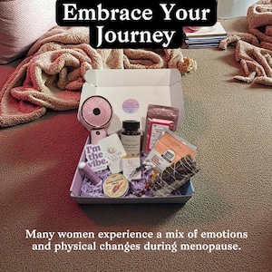 May include: An open gift box filled with self-care items, including a small fan, skincare products, and a candle. The box is on a brown surface, with text that reads "Embrace Your Journey" and "I'm the vibe."