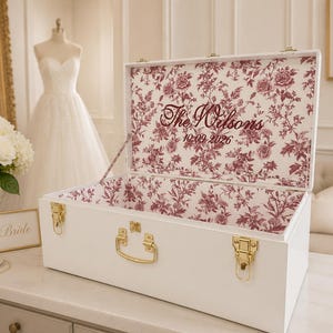 May include: A white rectangular wooden keepsake box with gold-toned metal latches and a handle. The interior lid and base feature a burgundy floral toile pattern. The text "The Wilsons" and "10.09.2026" is printed in burgundy on the inner lid.