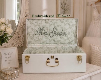 May include: A white rectangular storage chest with gold-toned metal latches and a handle. The interior is lined with a light green floral fabric. The inside lid features the embroidered text "Mrs. Gooden" and the text "Embroidered To last!"