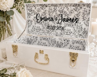 May include: A white rectangular wooden box with gold-toned metal latches and a handle. The interior lid and walls feature a black and white floral pattern. The text "Emma & James" and "10.22.2026" is printed in black on the inside of the lid.