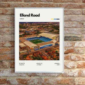 Puede incluir: Una impresión enmarcada que muestra una vista aérea del estadio Elland Road en Leeds. La impresión incluye el texto "Elland Road" y "LEEDS", con la capacidad del estadio y el año de apertura. El estadio tiene un campo azul y verde.