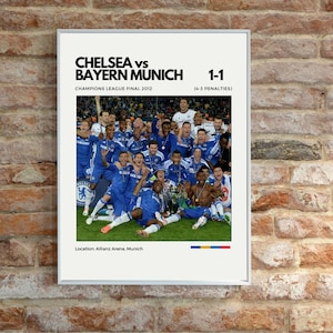 Può includere: Una stampa incorniciata con una fotografia della squadra di calcio del Chelsea che festeggia una vittoria. Il testo in alto recita "CHELSEA vs BAYERN MUNICH 1-1" e "CHAMPIONS LEAGUE FINAL 2012". Luogo: Allianz Arena, Monaco.