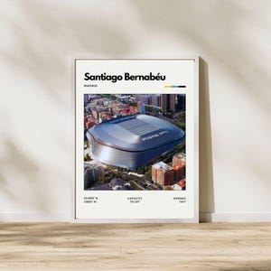 May include: A framed poster featuring an aerial view of the Santiago Bernabéu stadium in Madrid. The poster includes the stadium's name, location, and details about its capacity and opening year. The poster is set against a white background.