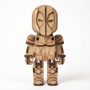 May include: A wooden Deadpool figure, standing upright, with a detailed design. The figure has a light brown color with darker brown accents, and features the character's mask and costume. The figure is a collectible item.