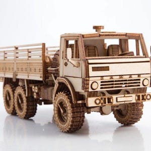 Puede incluir: Modelo de madera detallado de un camión KAMAZ, con seis ruedas, una caja de carga y una cabina del conductor. El modelo está construido con madera de color claro, mostrando detalles intrincados y un diseño realista. El modelo de camión es un objeto de colección.