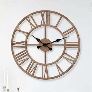 Puede incluir: Un reloj de pared grande y redondo con un marco de madera marrón claro y manecillas negras. El reloj presenta números romanos y un diseño minimalista, adecuado para la decoración del hogar. El diámetro del reloj es de aproximadamente 61 cm.