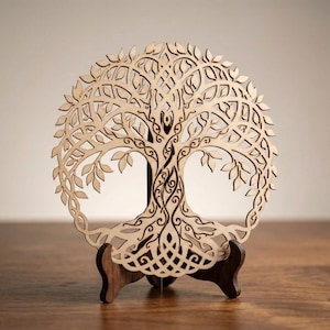 Puede incluir: Escultura de madera del Árbol de la Vida con intrincados detalles recortados. El árbol presenta un diseño circular con hojas, ramas y raíces, montado sobre un soporte de madera marrón oscuro. La obra de arte se exhibe sobre una superficie de madera.