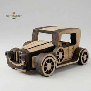 Może przedstawiać: Drewniany model zabytkowego samochodu, z dwutonowym wzorem z jasnego i ciemnobrązowego drewna. Samochód ma szczegółowe koła, charakterystyczny przedni grill i klasyczny styl nadwozia. Nazwa sklepu Etsy "VETRACUT" znajduje się w lewym górnym rogu.