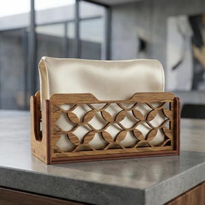May include: A wooden napkin holder with a decorative geometric pattern. The holder is made of light brown wood and contains a stack of cream-colored napkins. The design features a series of interlocking circles, adding a touch of elegance to the kitchen or dining area.