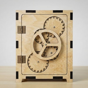 May include: Wooden safe with a gear mechanism. The safe is made of light-colored wood with a rectangular shape. The front features a large circular gear and several smaller gears. The hinges and accents are a darker wood. The safe is designed to be a puzzle.