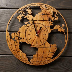 Könnte beinhalten: Eine Wanduhr aus Holz in Form einer Weltkarte. Das Zifferblatt ist kreisförmig mit schwarzen Zeigern und einem roten Sekundenzeiger. Die Uhr ist aus hellbraunem Holz gefertigt, mit einem dunkelbraunen Holz Hintergrund.
