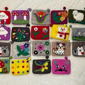 May include: A collection of colorful felt coin purses with various designs, including clouds, mushrooms, flowers, cats, and sheep. Each purse has a zipper and a small pom-pom attached. The purses are in shades of red, purple, yellow, gray, and green.