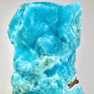 Può includere: Un vibrante esemplare di minerale blu strutturato. La struttura cristallina presenta un motivo radiale in alcune aree, con sfumature di blu chiaro e scuro. I bordi ruvidi e la forma naturale della pietra sono visibili.