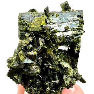 Op de afbeelding: Een close-up van een levendig groen mineraal specimen. De kristalstructuur toont een mix van donkere en lichtgroene tinten, met scherpe, hoekige formaties. Het mineraal heeft een reflecterende, bijna metallic glans.