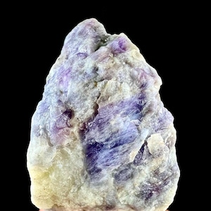 May include: A raw, unpolished mineral specimen featuring a combination of translucent white and deep purple crystalline structures. The stone has an irregular, jagged shape with a rough, textured surface showing natural mineral formations.