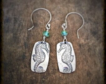 May include: Silver earrings with a seahorse design and green crystal accents.