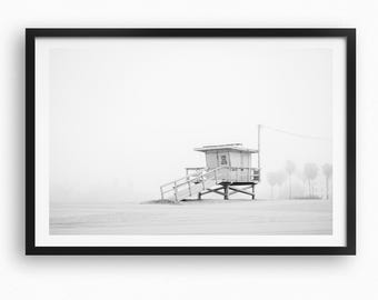 May include: Black and white framed print of a lifeguard stand on a beach. The stand is elevated with a small structure and a wooden ramp. The scene is set in a foggy environment, with a few trees visible in the background.