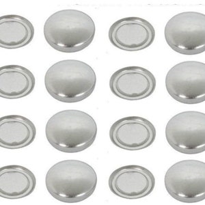Puede incluir: Un conjunto de dieciséis tapas metálicas plateadas, cada una con una parte superior abovedada y una base circular plana. Las tapas están dispuestas en un patrón de cuadrícula. Podrían ser sujetadores o elementos decorativos.