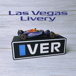 May include: A miniature Formula 1 race car with a red, yellow, and blue design, displayed on a black stand. The car features the Oracle logo and the text "Las Vegas Livery" above it.