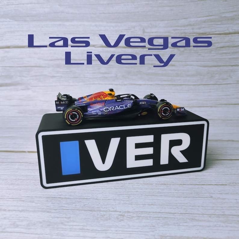May include: A miniature Formula 1 race car with a red, yellow, and blue design, displayed on a black stand. The car features the Oracle logo and the text "Las Vegas Livery" above it.