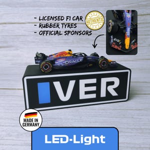 May include: A miniature Formula 1 race car with a blue and red design, featuring sponsor logos and the word "ORACLE". The car sits on a black base with the word "IVER" and a blue rectangle. The image includes text that says "LED-Light".
