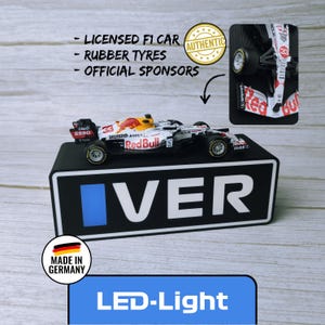 May include: A miniature Red Bull Formula 1 race car with the number 33, displayed on a black base with the word "VER". The car features sponsor logos and rubber tires. The image also includes the text "LED-Light" and "Made in Germany".