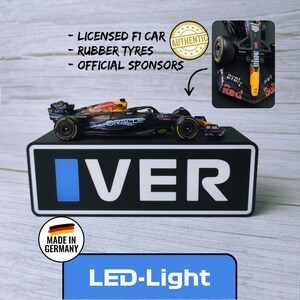 May include: A black and red F1 race car model with sponsor logos, rubber tires, and the text "ORACLE" and "VER". The model sits on a black base with the word "VER" in white. The image also includes the text "LED-Light".