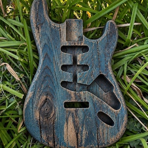 Pode incluir: Um corpo de guitarra elétrica inacabado feito de madeira com um acabamento de tinta azul desgastada. O corpo apresenta uma forma de corte duplo, um encaixe para o braço e cavidades fresadas para três captadores, uma ponte e um seletor.