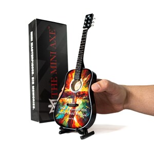 May include: A miniature acoustic guitar with a colorful abstract design, held on a black stand. The guitar features the text "What Is Impossible With Man Is Possible With God. Luke 18." A black box with "THE MINI AXE" is in the background.